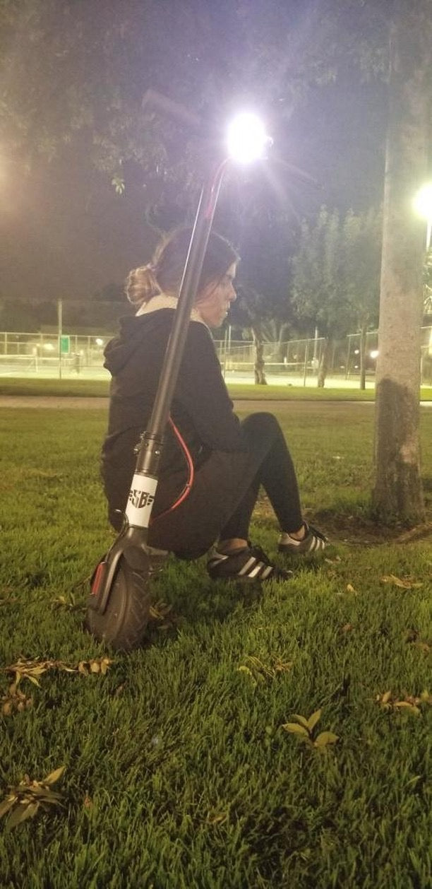 A rider sitting beside a scooter in a park at night under bright lights