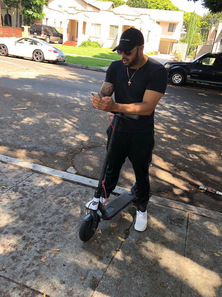 A rider checking a phone while standing with a scooter in a neighborhood street