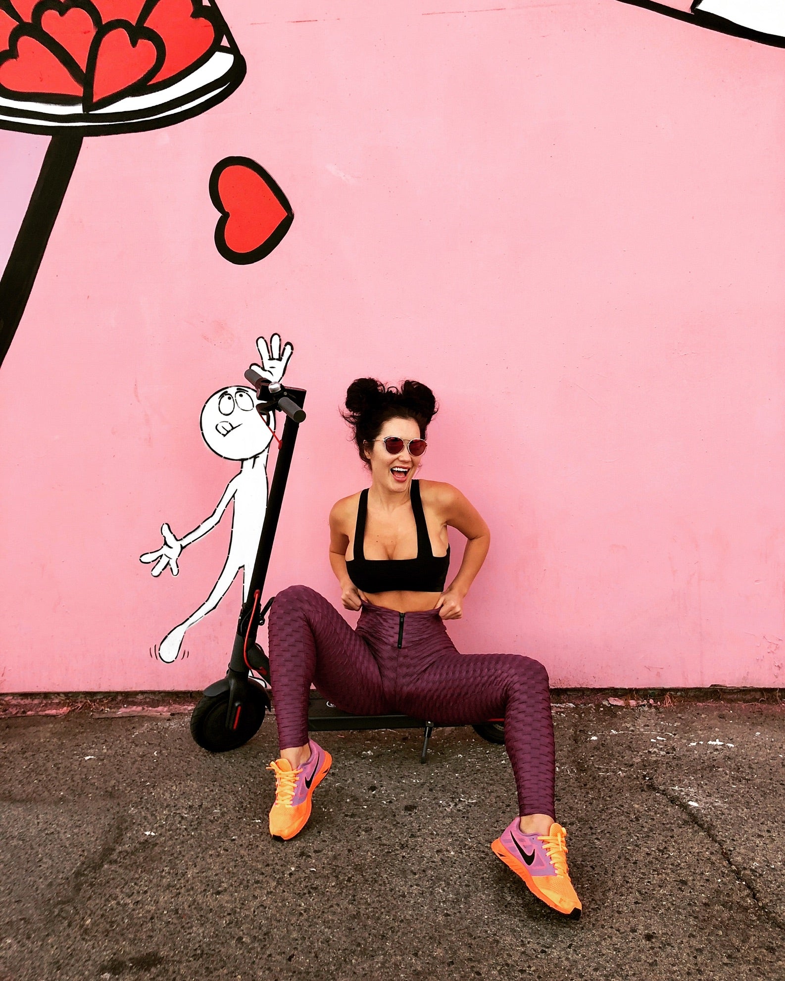 A rider posing with a scooter in front of a bright pink mural